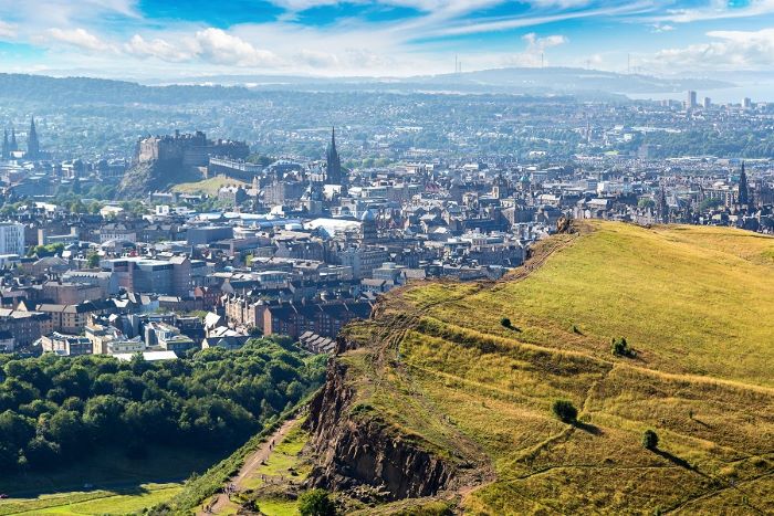View of Edinburgh from Arthur’s Seat, with the grassy cliffside pictured in front of the city skyline.