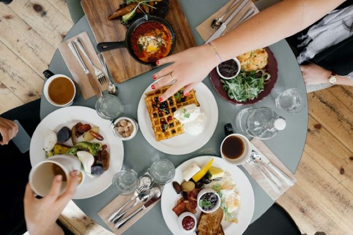 Group of friends having brunch, with hands reaching across the table to sample dishes.
