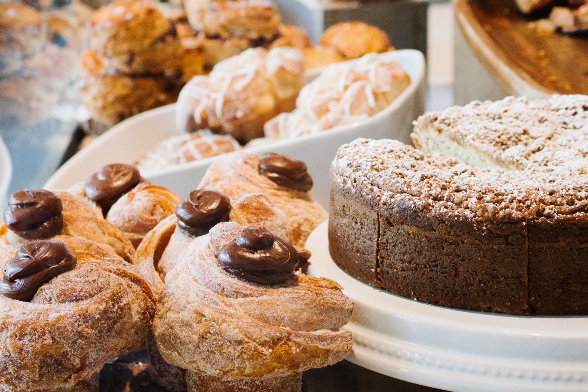 A large cake, pastries, and muffins lined up in a window display at a bakery.