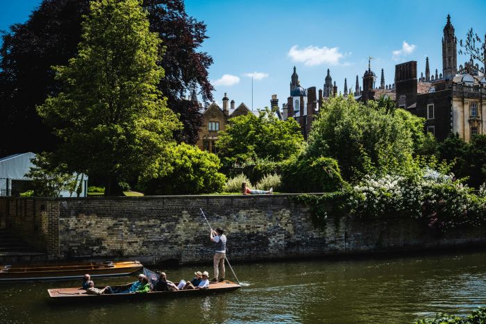 A group of people punting along the River Cam  on a clear, sunny day.
