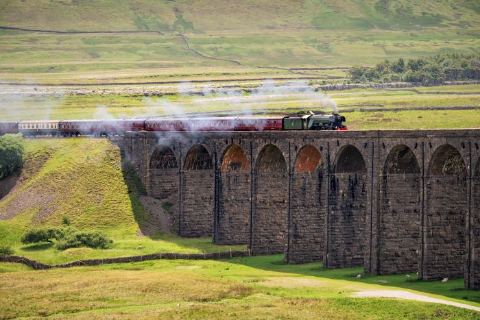 Flying Scotsman travels along a viaduct bridge in the Yorkshire Dales, with steam trailing from the engine.