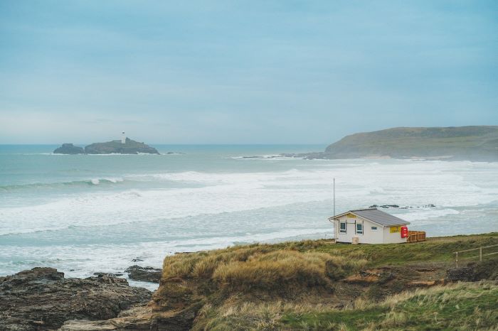 Godrevy Bay with rough blue waves, a lighthouse on an island, and a lifeguard hut.