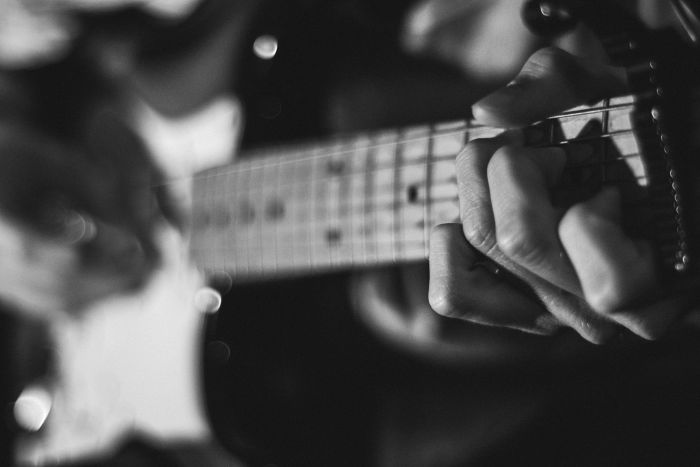 A person’s hands on a guitar playing chords, in black and white.