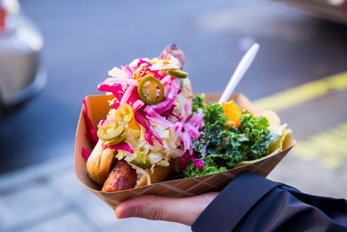 A hand holding a hot dog topped with jalapenos and vegetables.