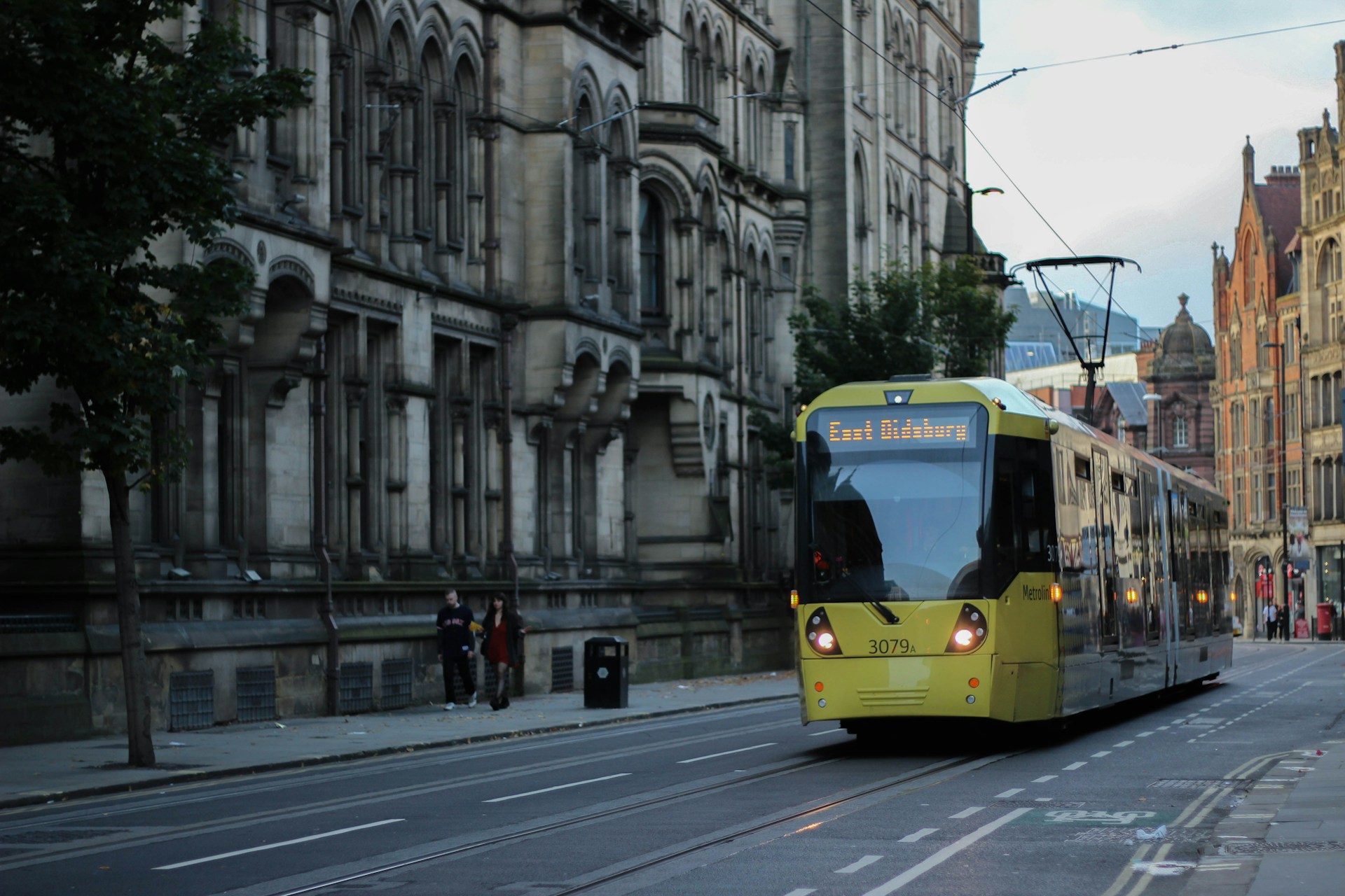 A yellow tram going through the streets of Manchester