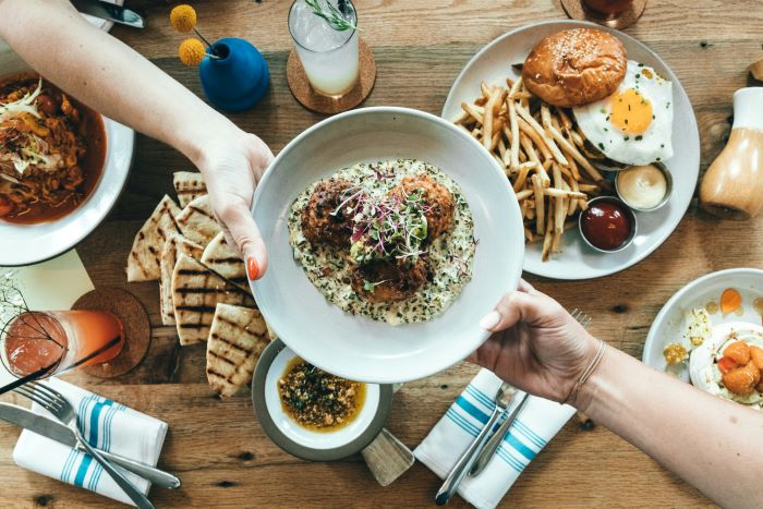 Two hands passing a plate of food, possible falafel, over a table.