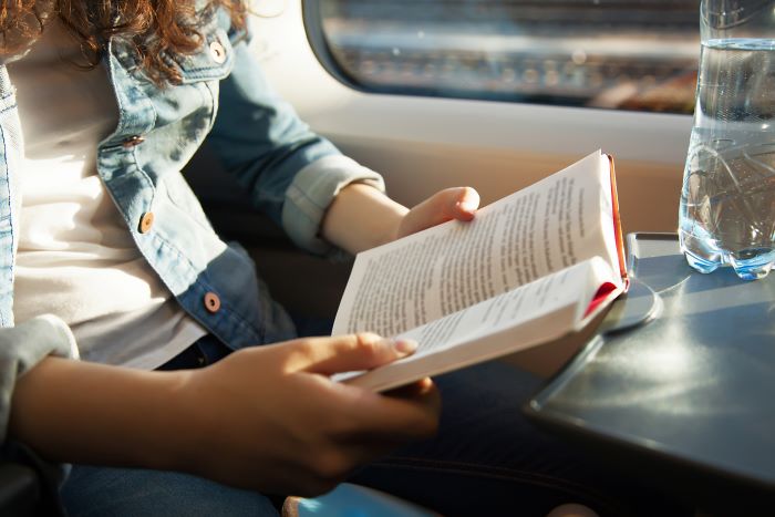 Person wearing a denim jacket reading a book on the train.
