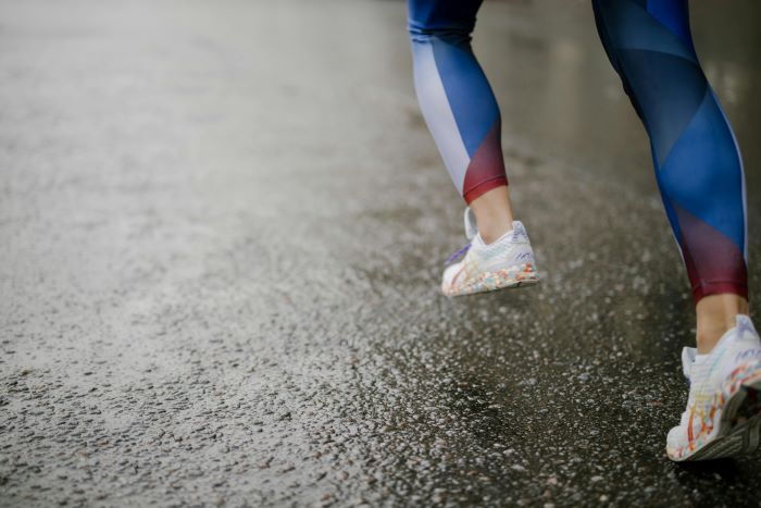 A person wearing running shoes and sports attire running along wet pavement.
