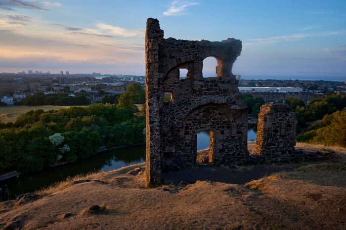 Ruins of St Anthony’s Chapel stand in Holyrood Park overlooking Edinburgh at dusk.